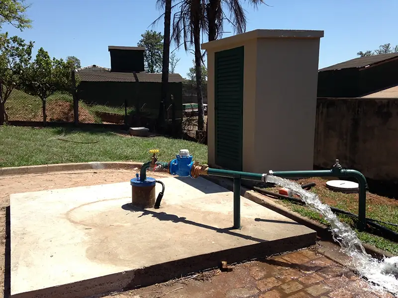 Poço concluído sobre uma laje de concreto, com a água saindo com força pela tubulação ao lado da casa de bombas